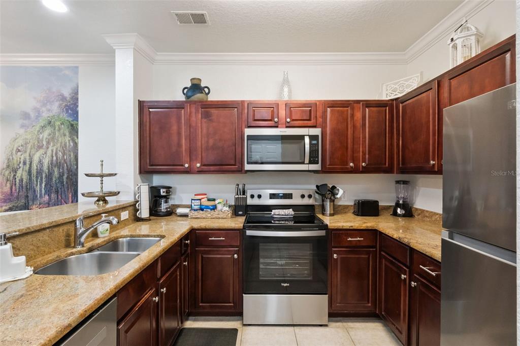 A kitchen features dark wood cabinets, granite countertops, and stainless steel appliances — 1351 TUSCAN TERRACE UNIT 8301, DAVENPORT, FL