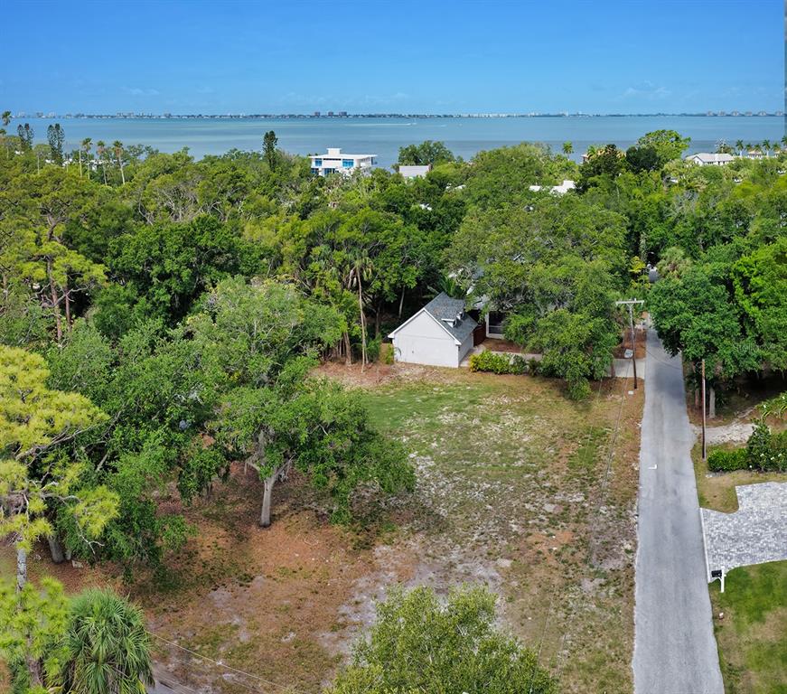 An aerial view shows a vacant lot with trees next to a house and road — TURKS CAP PLACE, SARASOTA, FL