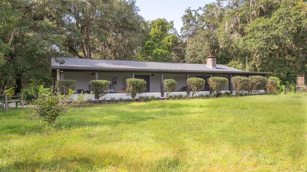 A single-story house with a long front porch sits on a grassy lot with trees — 22304 NE 35TH AVENUE, MELROSE, FL