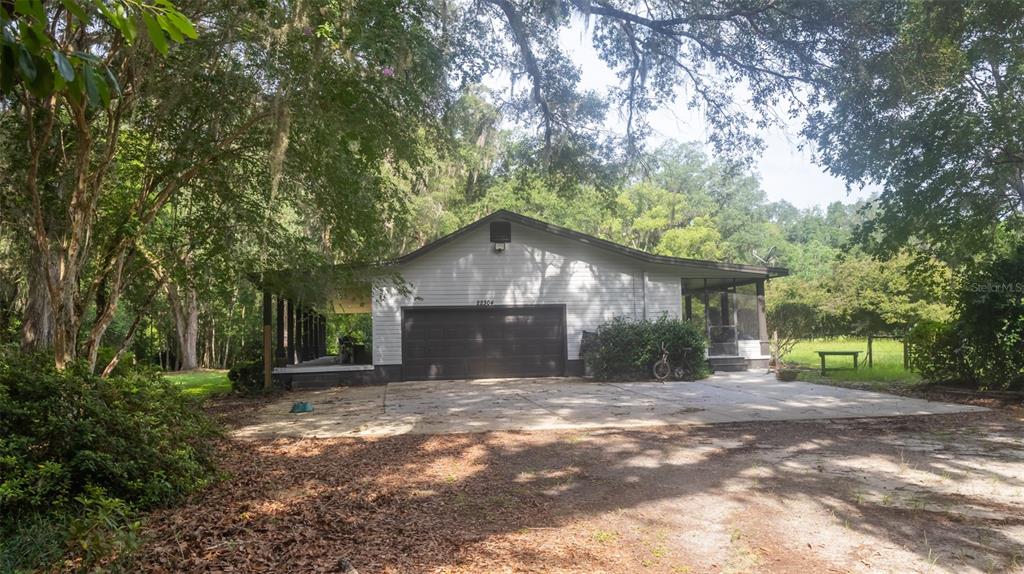 A white house with a dark garage door and a covered porch sits among trees — 22304 NE 35TH AVENUE, MELROSE, FL