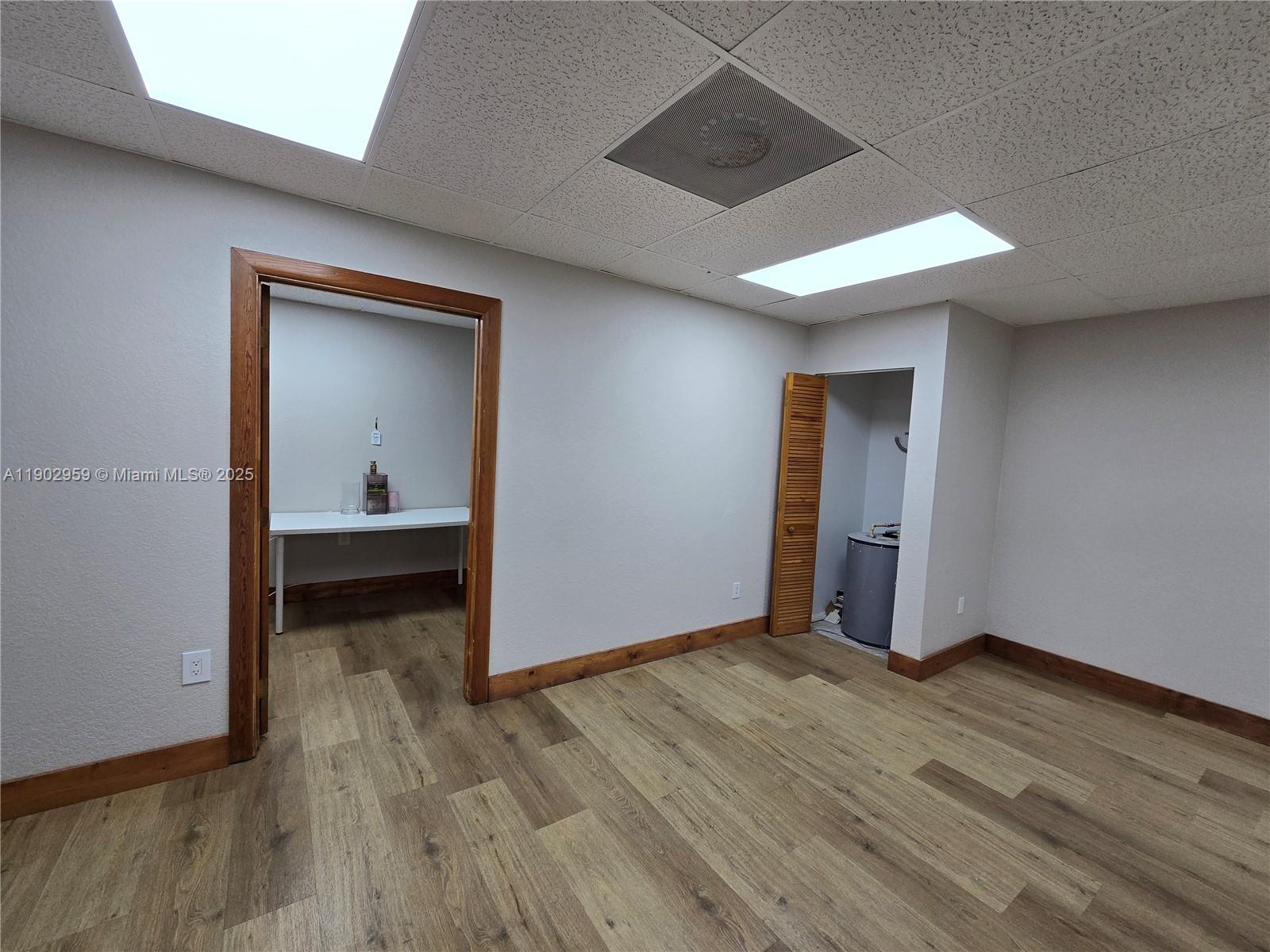 An empty room features wood-look flooring, a drop ceiling, and two doorways leading to smaller spaces — 3580 NW 32nd St, Miami FL 33142, MIAMI, FL