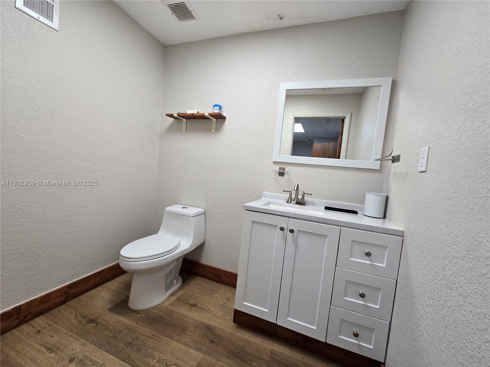 A bathroom features a white vanity, a toilet, a wall-mounted shelf, and wood-look flooring — 3580 NW 32nd St, Miami FL 33142, MIAMI, FL