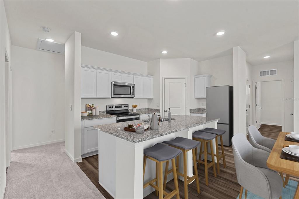A kitchen features white cabinets, granite countertops, a center island with bar stools, and appliances — 36094 CANELLI WAY, DADE CITY, FL