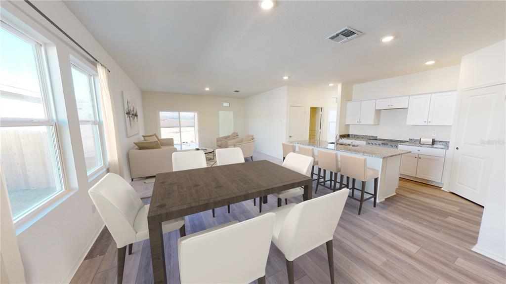 An open-concept dining area and kitchen with white cabinets, granite countertops, and wood-look flooring — 36094 CANELLI WAY, DADE CITY, FL