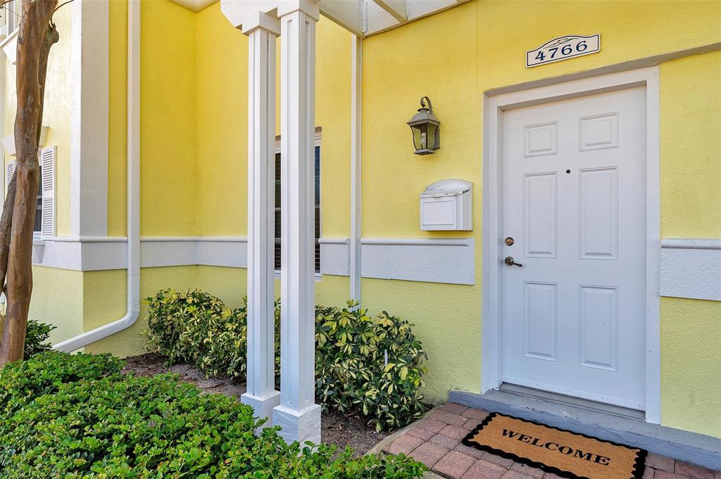 A yellow exterior wall features a white door, a mailbox, and a welcome mat — 4766 SNOOK DRIVE SE, ST PETERSBURG, FL