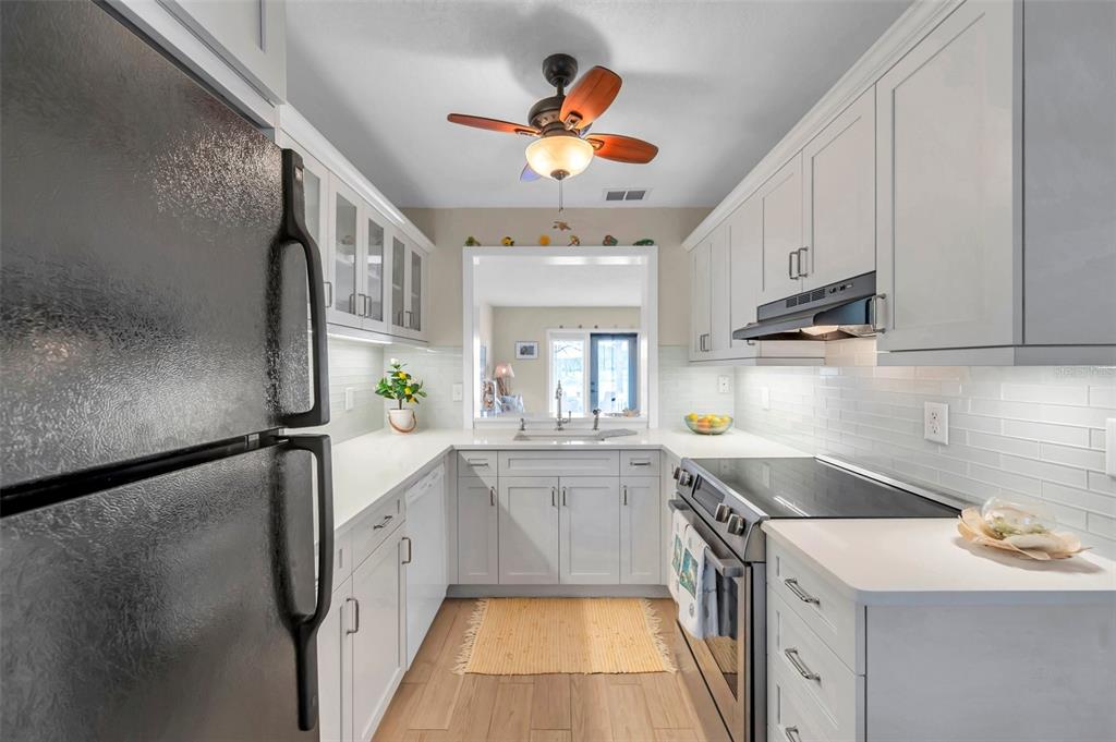 A galley kitchen features white cabinets, light countertops, stainless steel appliances, and a pass-through window — 4766 SNOOK DRIVE SE, ST PETERSBURG, FL