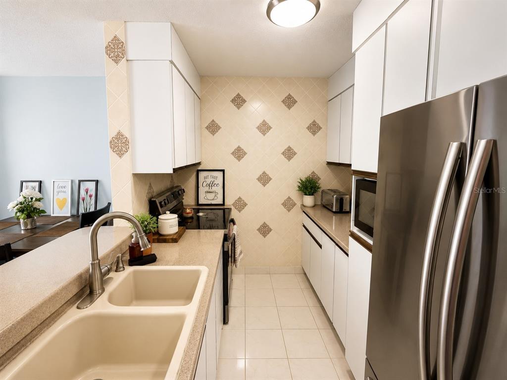 A galley kitchen features white cabinets, beige tile backsplash, stainless steel appliances, and a double sink — 3 OCEAN DR. UNIT 201, LUQUILLO, PR