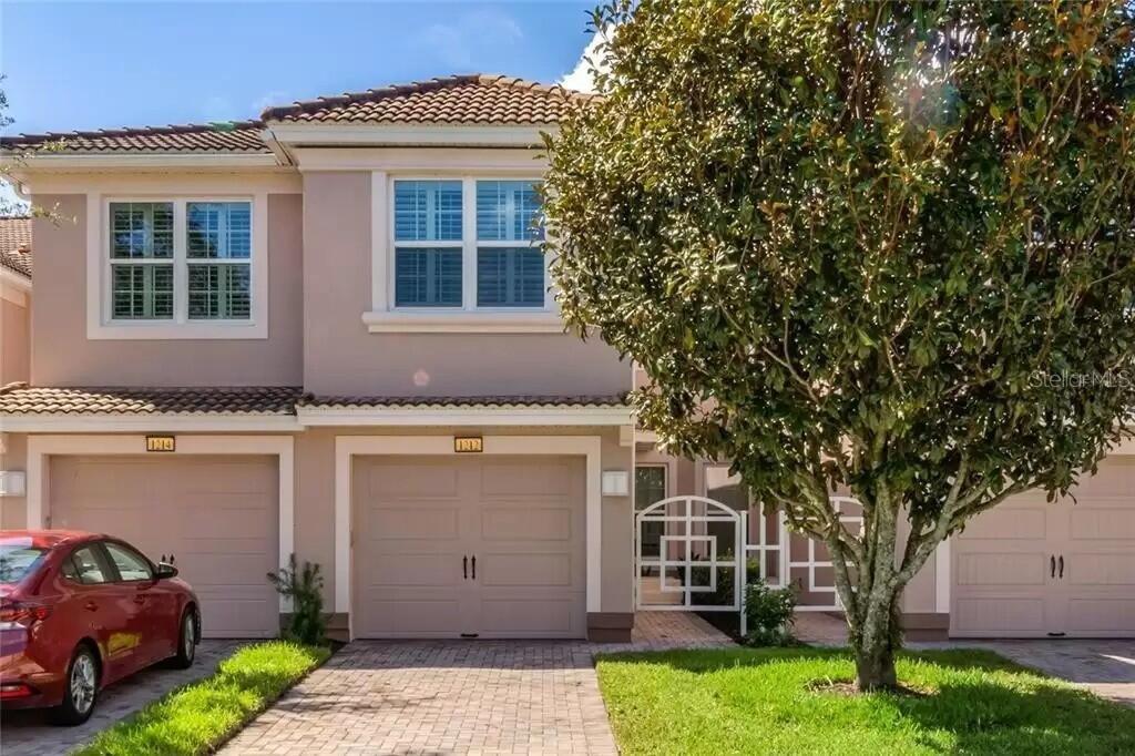 A two-story townhouse exterior features two garage doors, a paved driveway, and a large tree — 1212 ROMANI AVENUE, DAVENPORT, FL