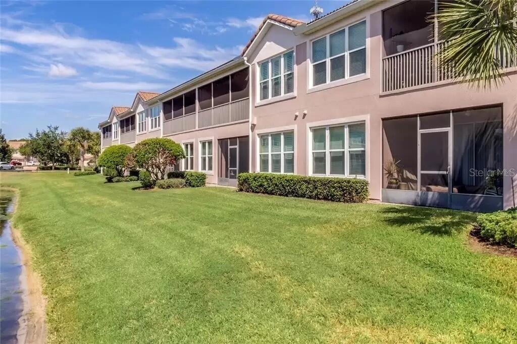 A multi-story residential building with screened-in balconies and patios overlooking a grassy lawn and pond — 1212 ROMANI AVENUE, DAVENPORT, FL