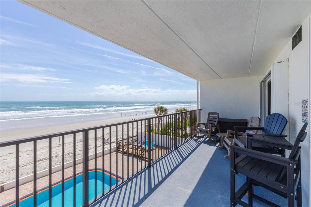 A balcony with outdoor seating overlooks a swimming pool and the sandy beach — 3807 S ATLANTIC AVENUE UNIT 302, DAYTONA BEACH, FL