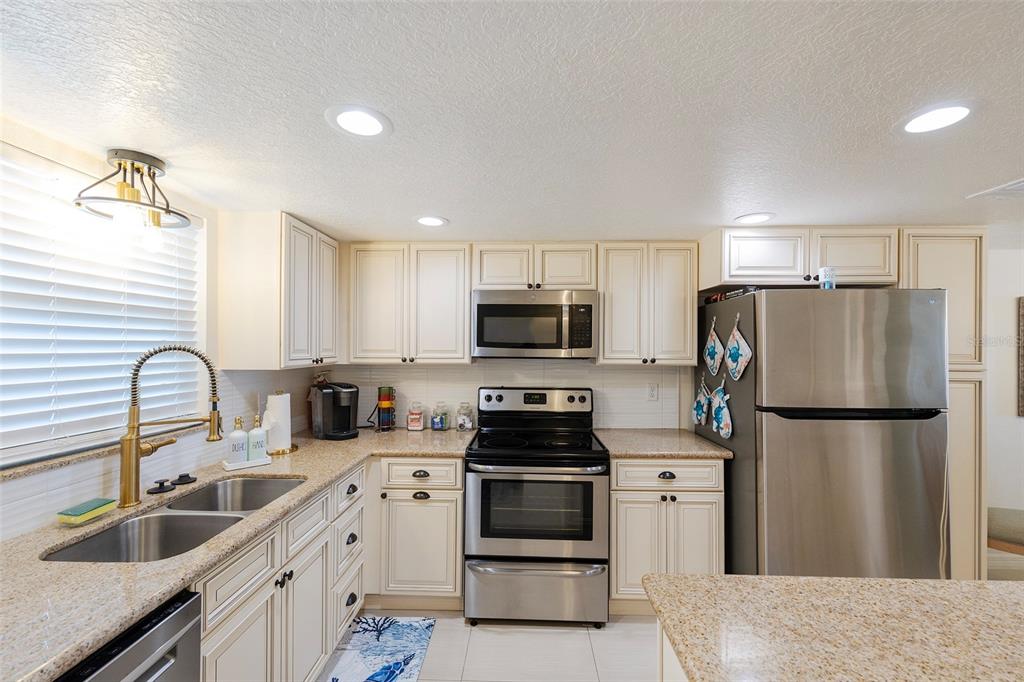 A kitchen features cream-colored cabinets, granite countertops, stainless steel appliances, and a double-basin sink — 3807 S ATLANTIC AVENUE UNIT 302, DAYTONA BEACH, FL