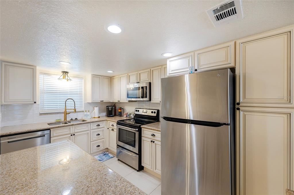 A kitchen with stainless steel appliances, cream-colored cabinets, and granite countertops — 3807 S ATLANTIC AVENUE UNIT 302, DAYTONA BEACH, FL