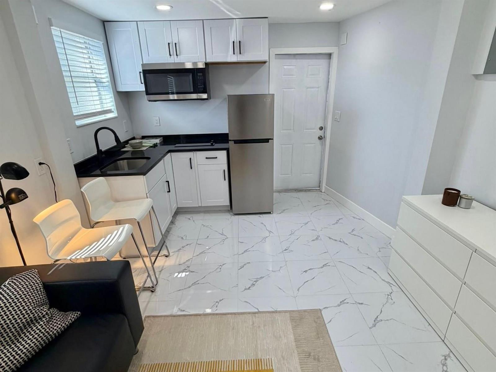 A small kitchen features white cabinets, black countertops, stainless steel appliances, and white marble-patterned flooring — 851 NW 4th Avenue, Pompano Beach FL 33060, POMPANO BEACH, FL