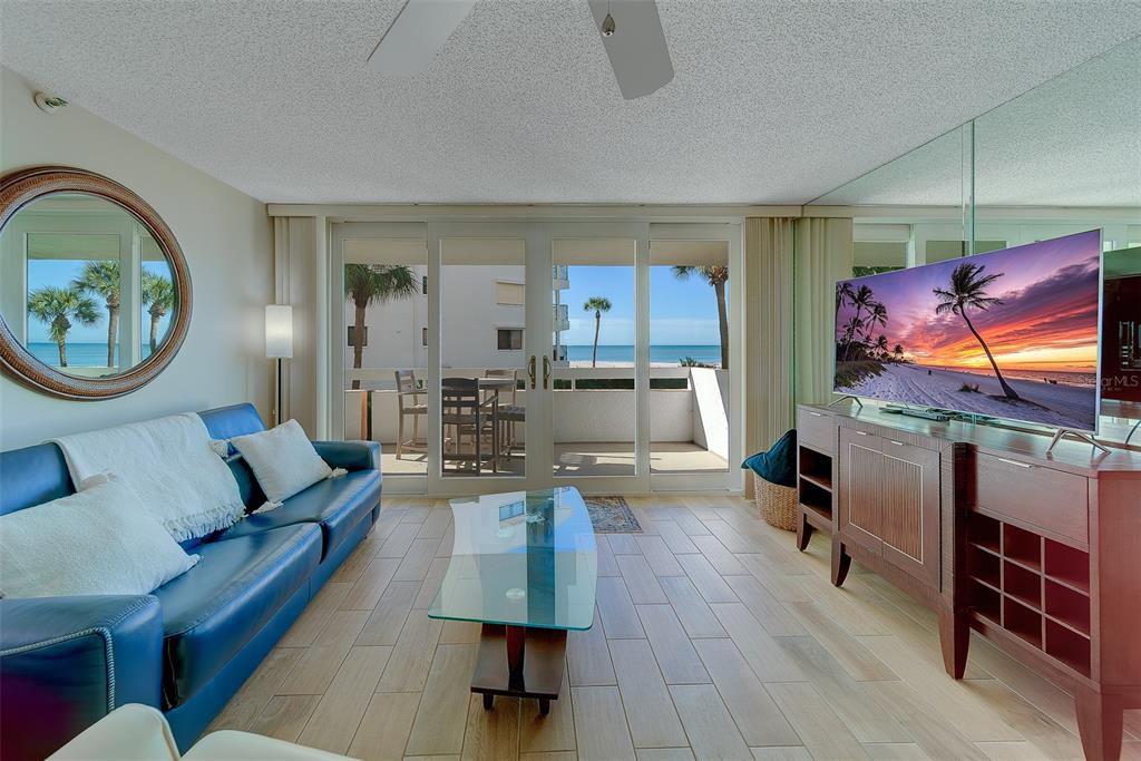 A living room features a blue sofa, glass coffee table, and sliding doors to a balcony — 17900 GULF BOULEVARD UNIT 1B, REDINGTON SHORES, FL