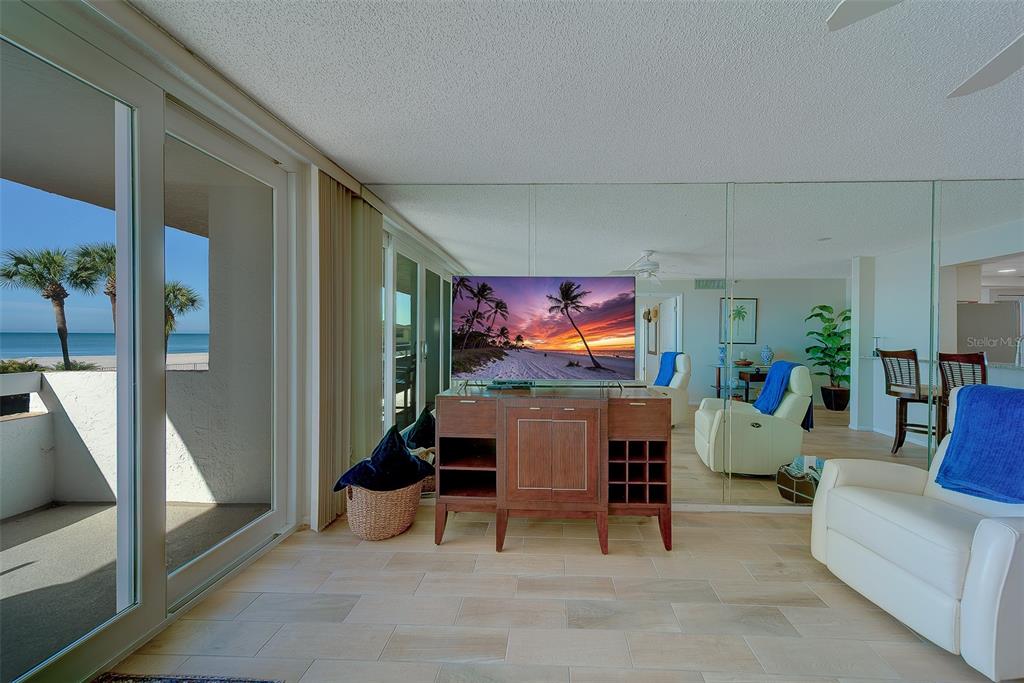 A living room features a TV on a wooden console, tiled floors, and mirrored walls — 17900 GULF BOULEVARD UNIT 1B, REDINGTON SHORES, FL