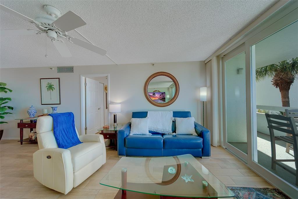 A living room features a blue sofa, white recliner, glass coffee table, and sliding glass doors — 17900 GULF BOULEVARD UNIT 1B, REDINGTON SHORES, FL