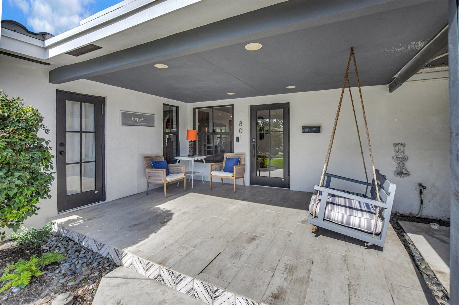 A covered patio features light-colored tile flooring, two chairs with a table, and a hanging swing — 801 SW 5th Street, Boca Raton FL 33486, BOCA RATON, FL