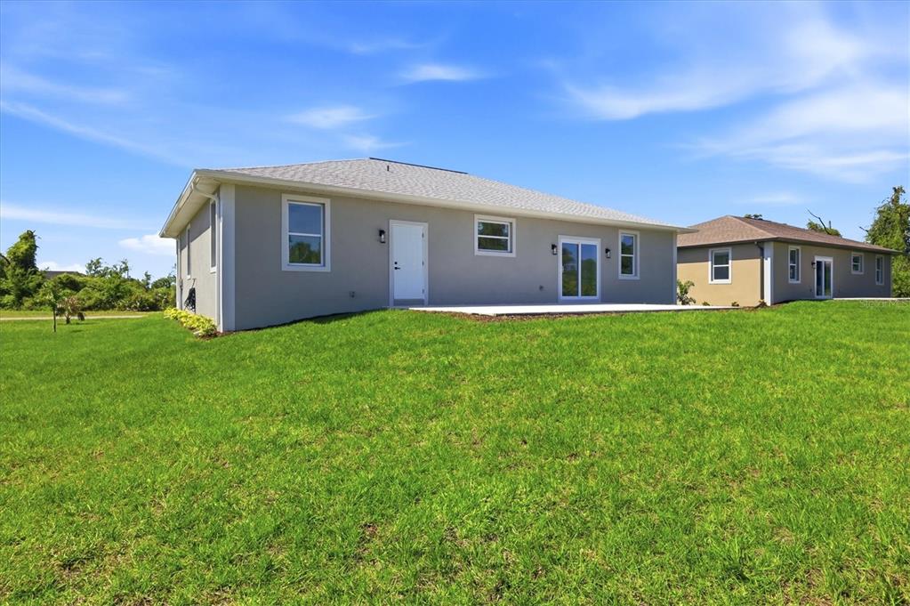 The exterior rear view of a single-story house with a concrete patio and green lawn — 8 BANK COURT, PLACIDA, FL