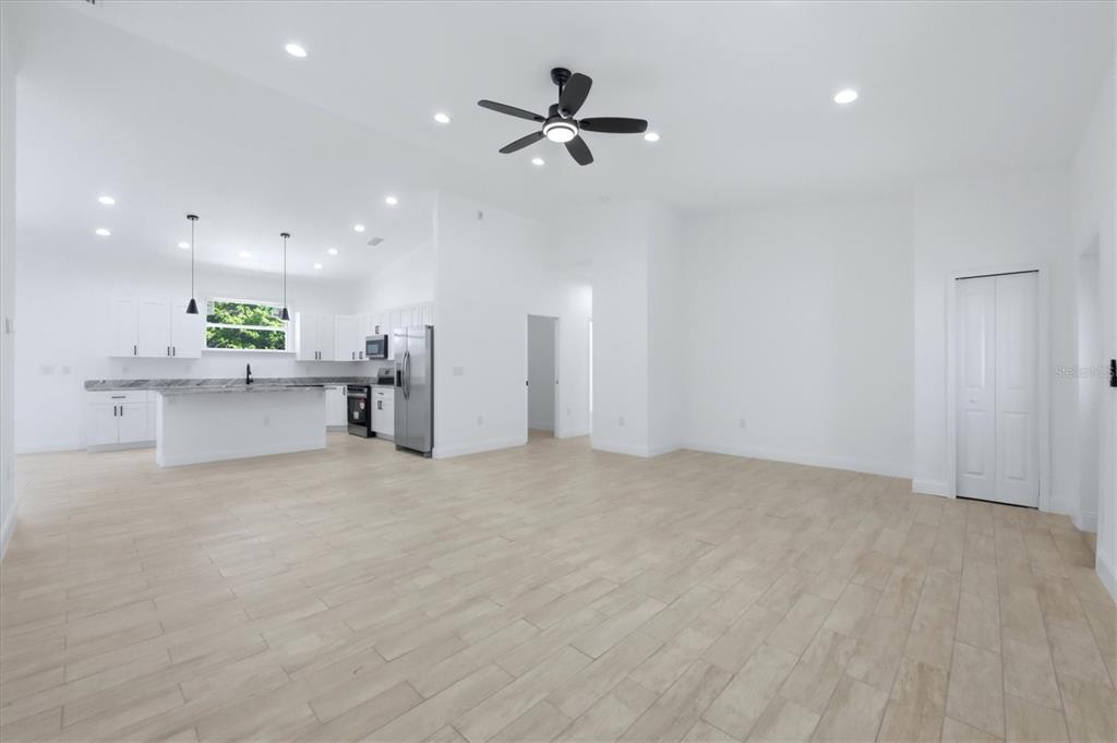 A bright, open-concept kitchen and living area with white cabinets and light wood-look flooring — 8 BANK COURT, PLACIDA, FL