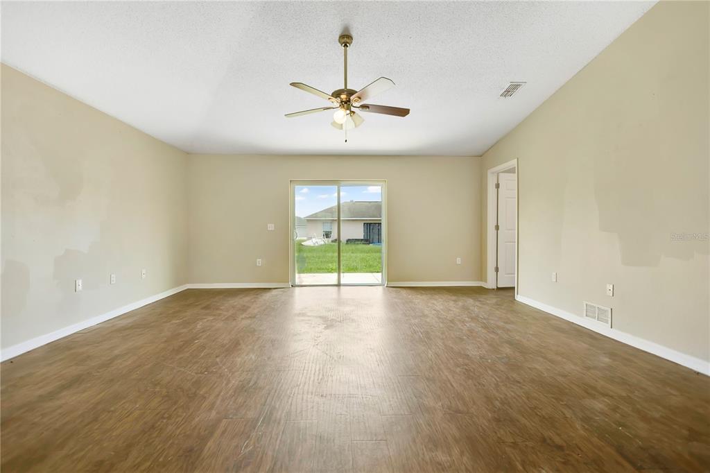 An empty living room features wood-look flooring, beige walls, a ceiling fan, and sliding glass doors — 3941 WARBLER DRIVE, WINTER HAVEN, FL