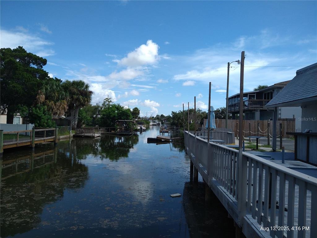 A canal view featuring wooden docks, palm trees, and a residential building under a blue sky — 6920,6922,6924,6926,6928 CLARK STREET, HUDSON, FL