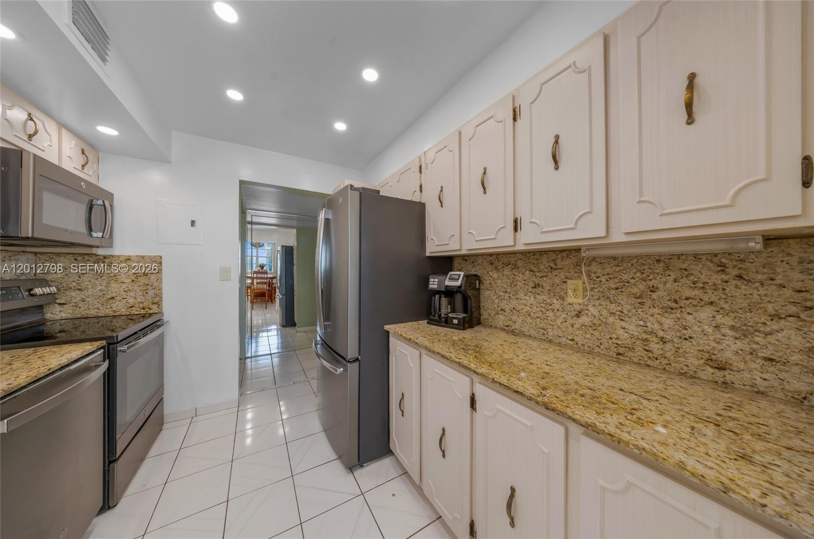 A kitchen features light-colored cabinets, granite countertops, stainless steel appliances, and white tile flooring — 3113 S Ocean Dr # 506, Hallandale Beach FL 33009, HALLANDALE BEACH, FL