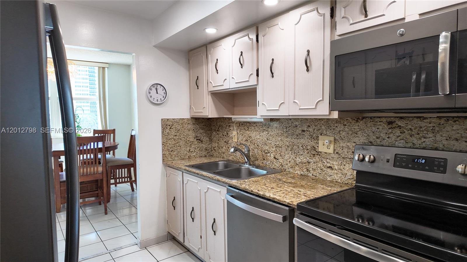 A kitchen features granite countertops, light-colored cabinets, stainless steel appliances, and a dining area beyond — 3113 S Ocean Dr # 506, Hallandale Beach FL 33009, HALLANDALE BEACH, FL
