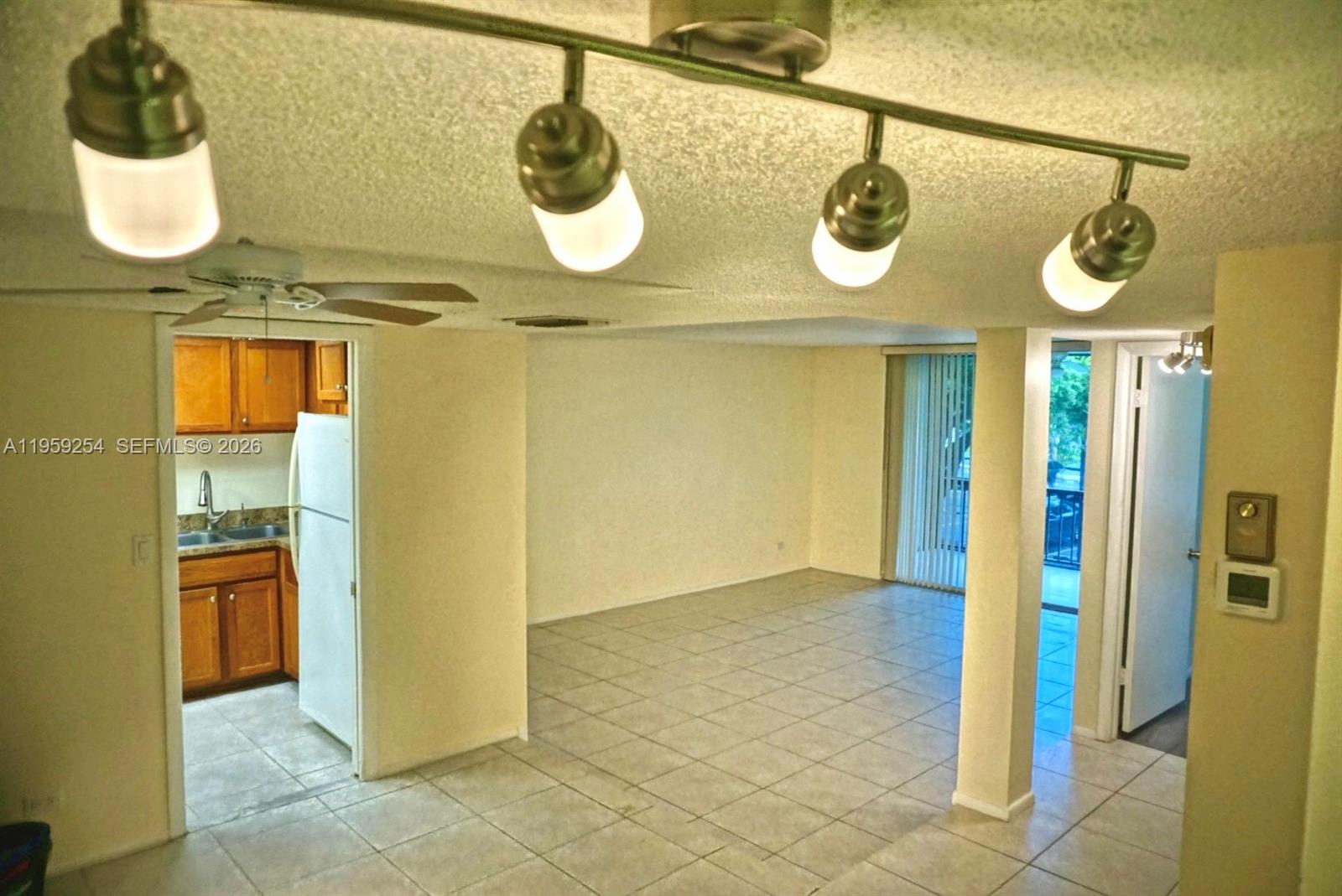 An interior view shows a tiled living area with a track lighting fixture and kitchen — 3740 Inverrary Dr # 2N, Lauderhill FL 33319, LAUDERHILL, FL