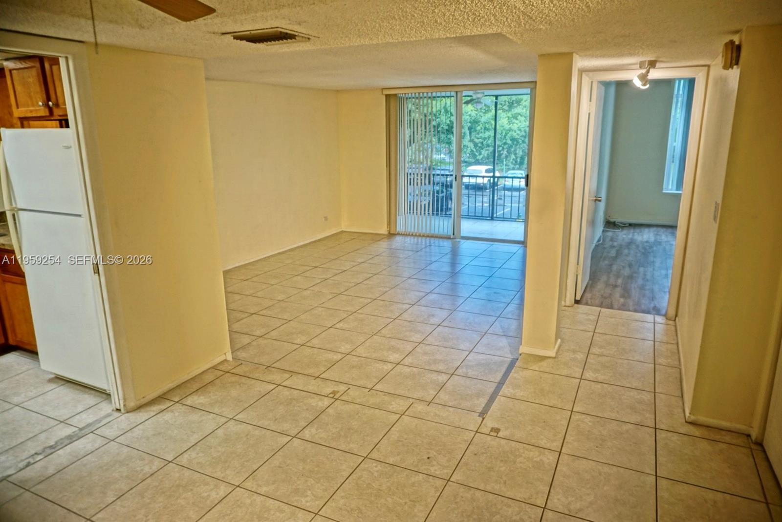 An empty living area features light-colored tile flooring and a sliding glass door to a balcony — 3740 Inverrary Dr # 2N, Lauderhill FL 33319, LAUDERHILL, FL