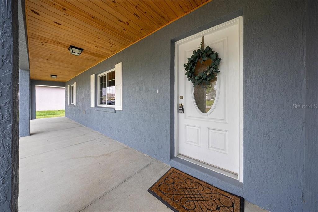 A covered concrete porch features a white front door with a wreath and wood-paneled ceiling — 15675 SE 89TH TERRACE, SUMMERFIELD, FL