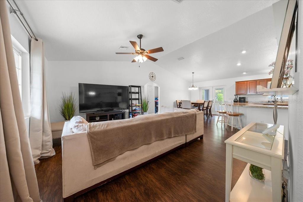 A living room with a large sofa, television, and an open-concept kitchen in the background — 15675 SE 89TH TERRACE, SUMMERFIELD, FL