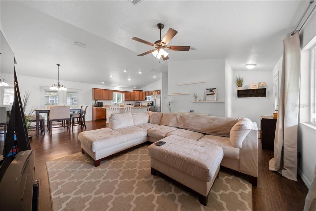 A living room with a large sectional sofa, an ottoman, and an open-concept kitchen — 15675 SE 89TH TERRACE, SUMMERFIELD, FL