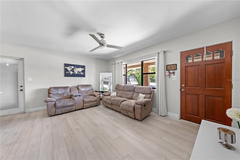 A living room features light wood-look flooring, two brown reclining sofas, and a wooden front door — 1712 PATRICK STREET, KISSIMMEE, FL