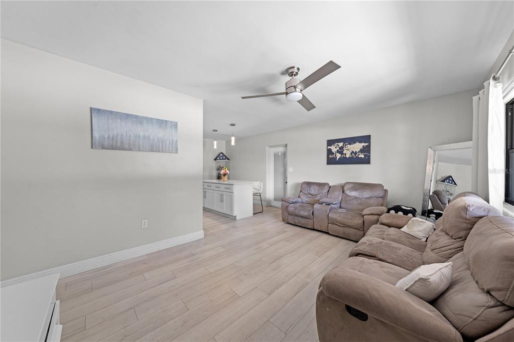 A living room with light wood-look flooring, a ceiling fan, and two brown reclining sofas — 1712 PATRICK STREET, KISSIMMEE, FL