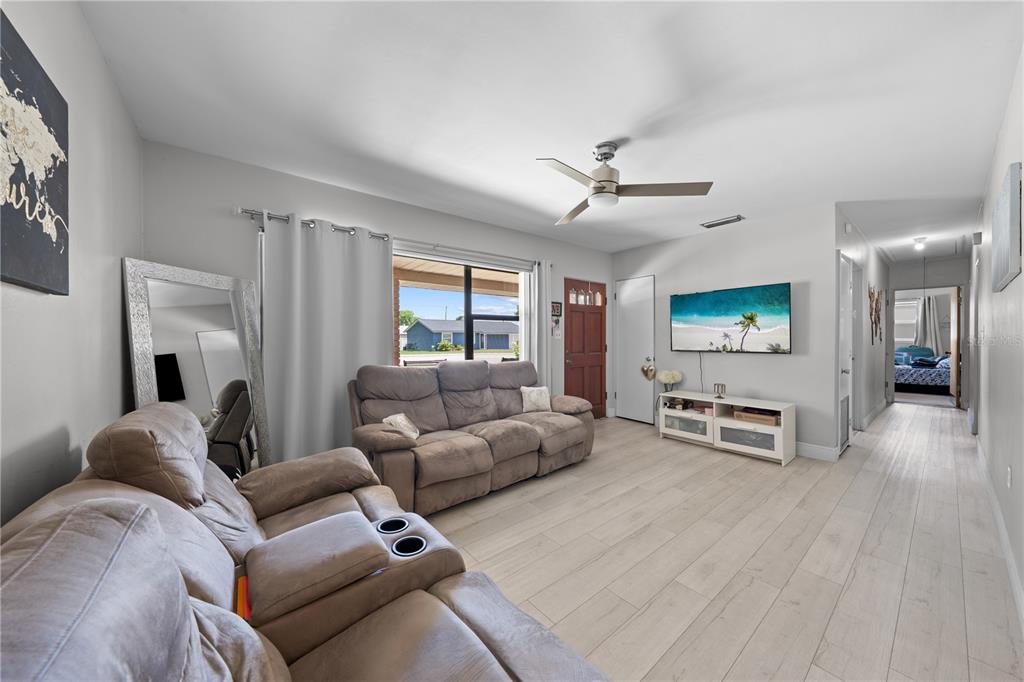 A living room features light wood-look flooring, a ceiling fan, and two brown reclining sofas — 1712 PATRICK STREET, KISSIMMEE, FL