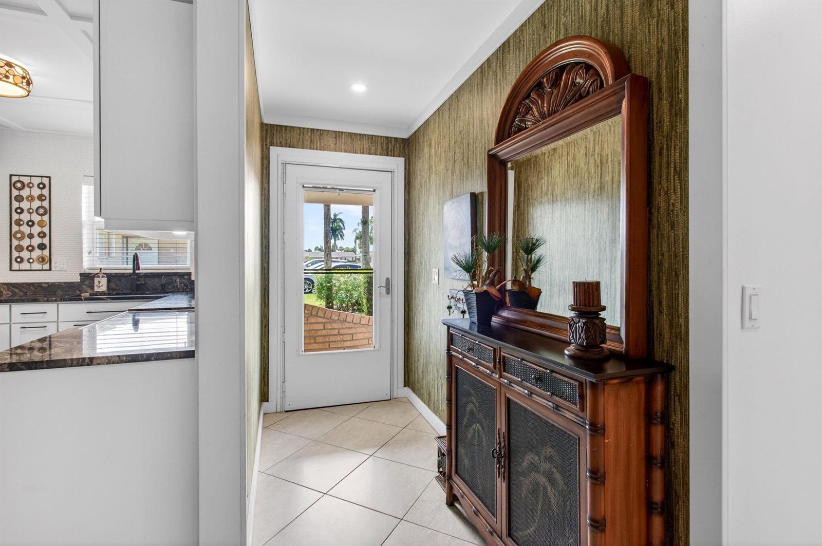 An entryway with tile flooring, textured wallpaper, and a wooden console table with a mirror — 2533 Dudley Dr, West Palm Beach FL 33415, WEST PALM BEACH, FL