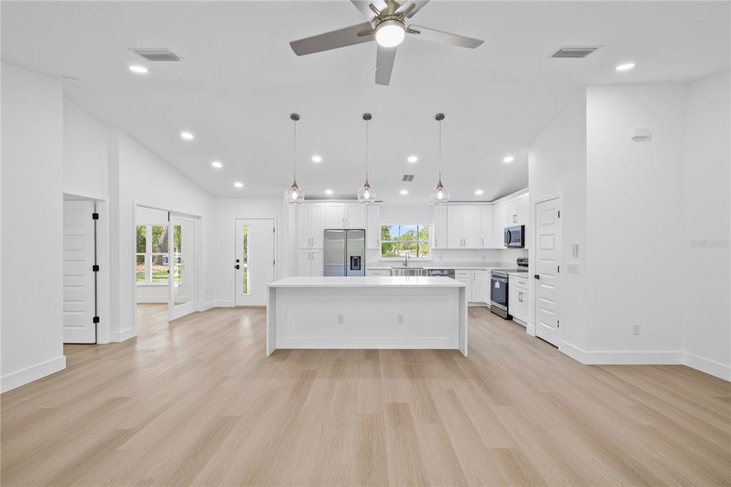 A bright, open-concept kitchen features a central island, white cabinetry, and light wood flooring — 8157 N VOYAGER DRIVE, CITRUS SPRINGS, FL