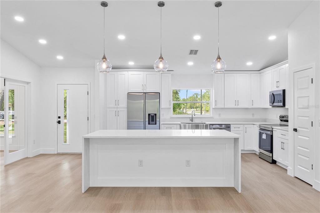 A modern white kitchen features a central island, stainless steel appliances, and light wood flooring — 8157 N VOYAGER DRIVE, CITRUS SPRINGS, FL