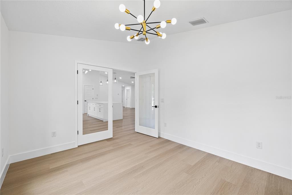 An empty room with light wood floors, white walls, and French doors leading to a kitchen — 8157 N VOYAGER DRIVE, CITRUS SPRINGS, FL