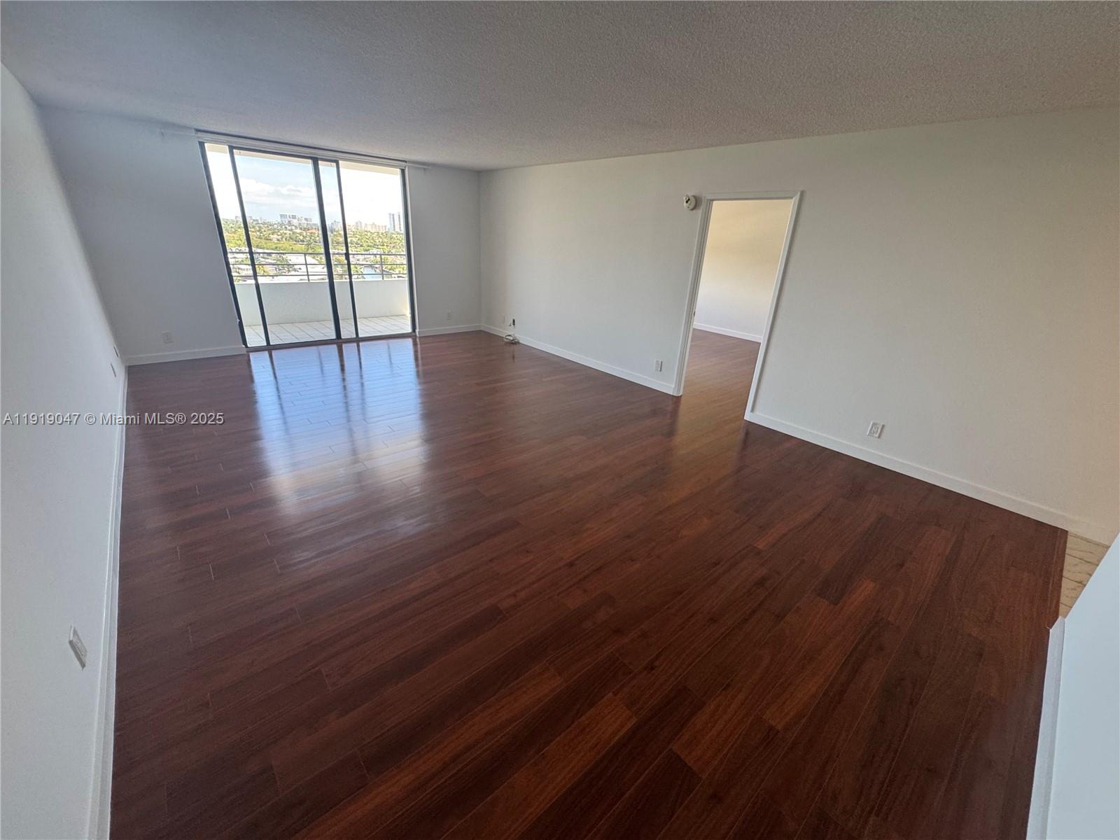 An empty living room features dark wood flooring, white walls, and a sliding glass balcony door — 2500 Parkview Dr # 1109, Hallandale Beach FL 33009, HALLANDALE BEACH, FL
