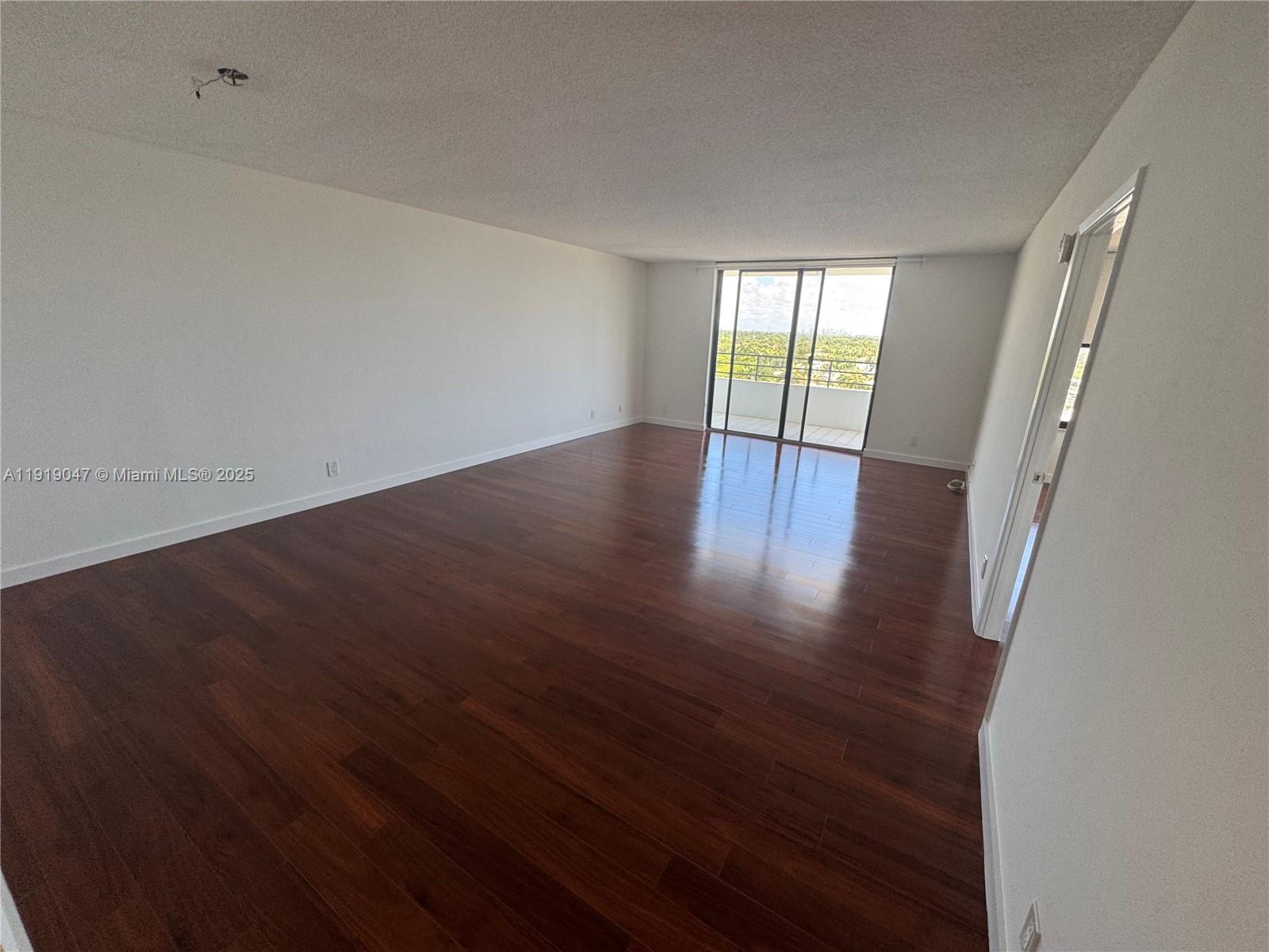An empty room with dark wood flooring, white walls, and a sliding glass balcony door — 2500 Parkview Dr # 1109, Hallandale Beach FL 33009, HALLANDALE BEACH, FL