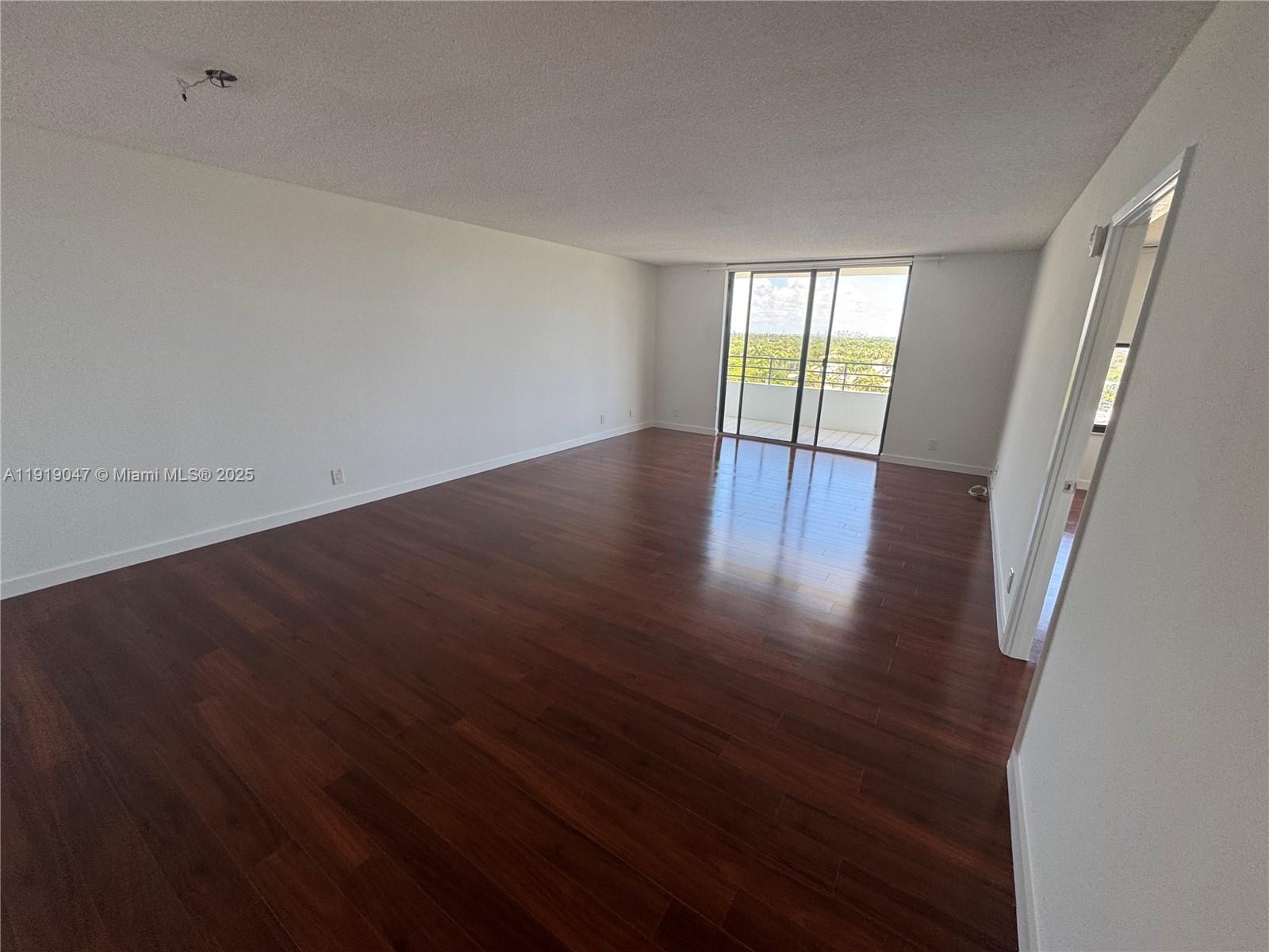 An empty room features dark wood flooring, white walls, and a sliding glass balcony door — 2500 Parkview Dr # 1109, Hallandale Beach FL 33009, HALLANDALE BEACH, FL