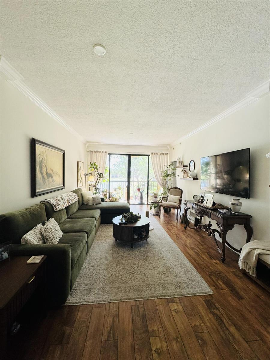 A living room features a green sectional sofa, a round coffee table, and a wall-mounted television — 6720 Coral Lake Drive # 6720, Margate FL 33063, MARGATE, FL