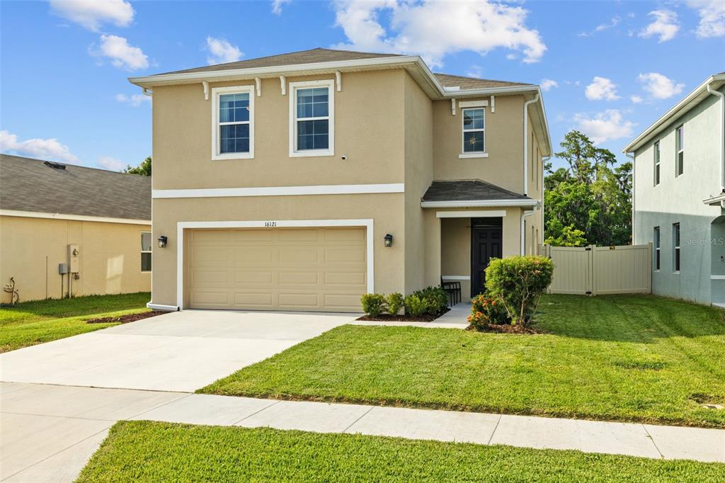 A two-story tan stucco house features a two-car garage and a small front porch — 16121 SOFT FERN TRACE, ODESSA, FL