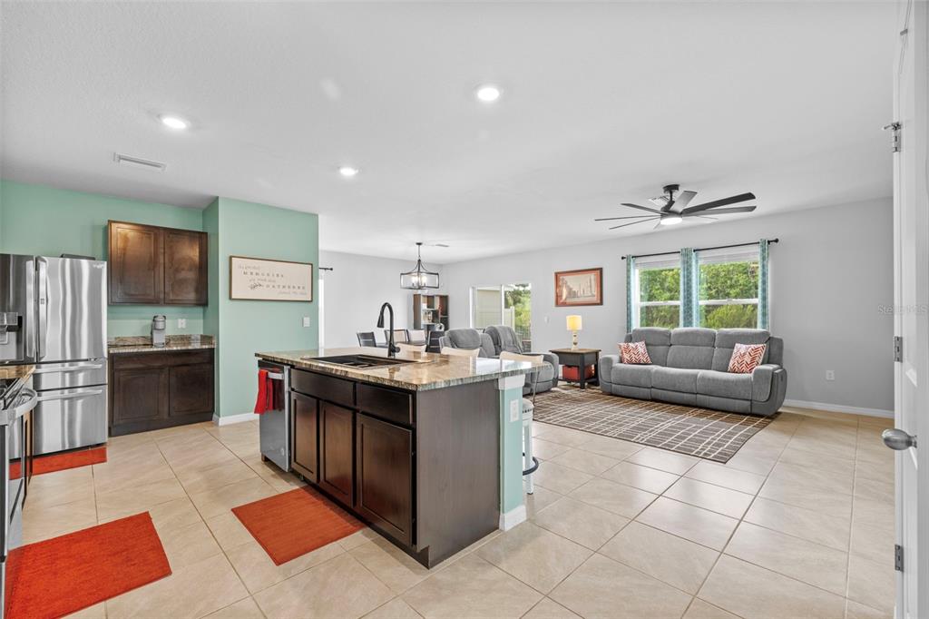 An open-concept kitchen with dark cabinets and a granite island overlooks a living room area — 16121 SOFT FERN TRACE, ODESSA, FL