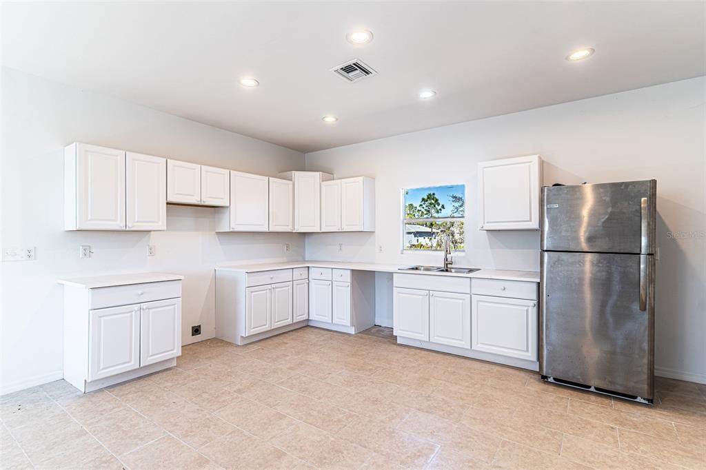 A kitchen with white cabinets, stainless steel refrigerator, light tile flooring, and recessed lighting — 1406 BITTERSWEET STREET, LAKE PLACID, FL