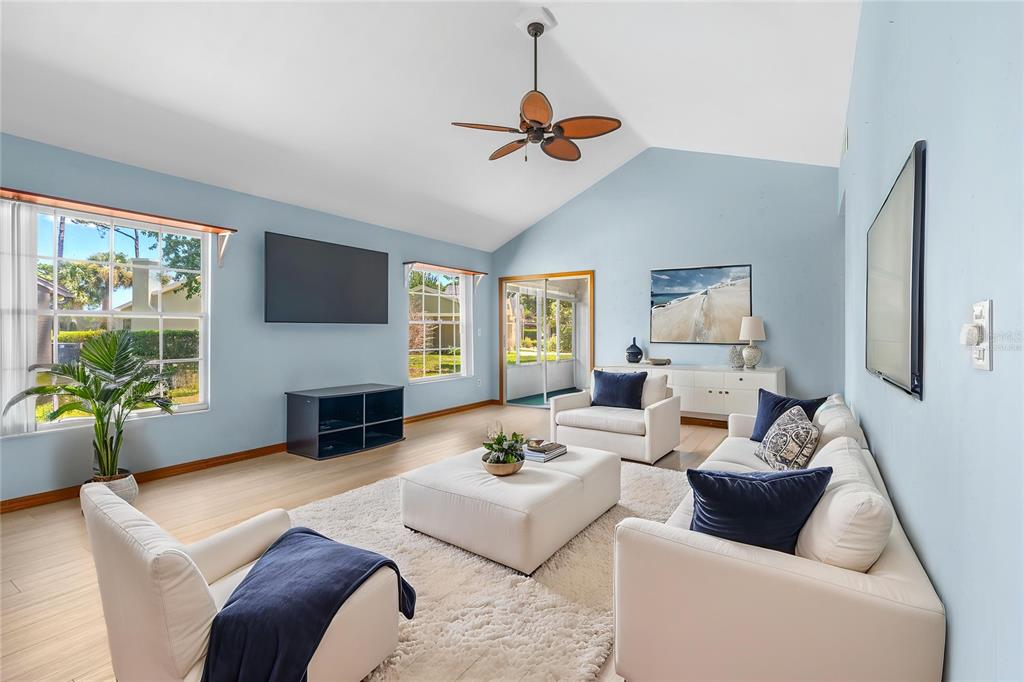 A living room with light blue walls, a vaulted ceiling, and white furniture on a rug — 104 SHOAL CREEK CIRCLE, DAYTONA BEACH, FL
