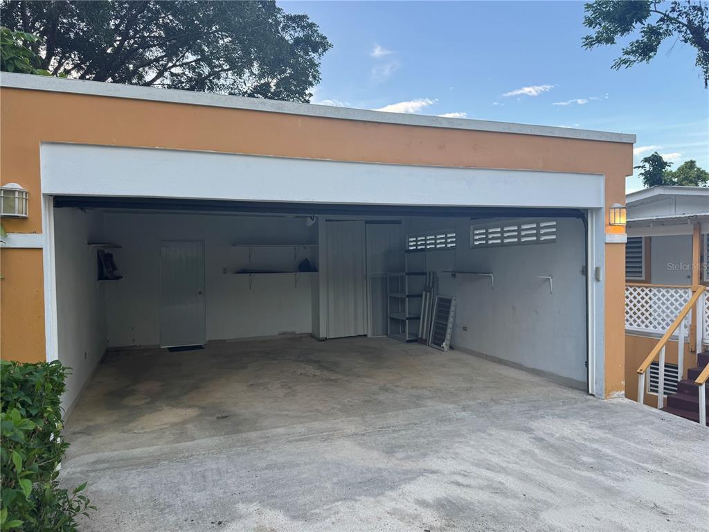 An open-air garage with concrete flooring, white walls, storage shelving, and a side door — 17 G23 COLINAS DEL YUNQUE, RIO GRANDE, PR