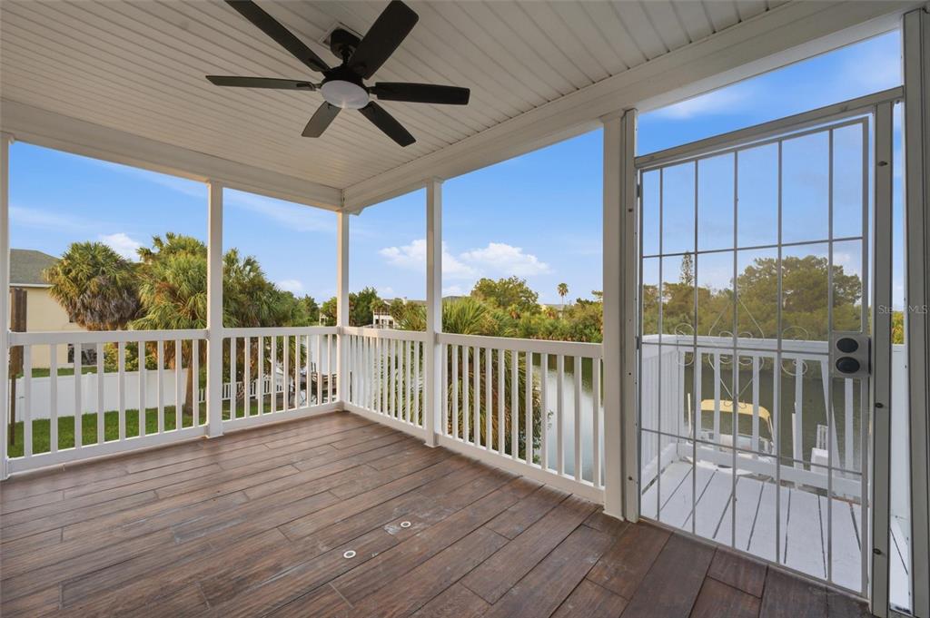 A covered balcony with wood-look tile flooring, white railings, a ceiling fan, and a screen door — 3316 HOLLY SPRINGS DRIVE, HERNANDO BEACH, FL