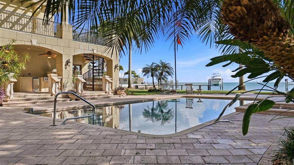A swimming pool sits on a stone patio beside a house with a spiral staircase — 6755 30TH STREET S, ST PETERSBURG, FL